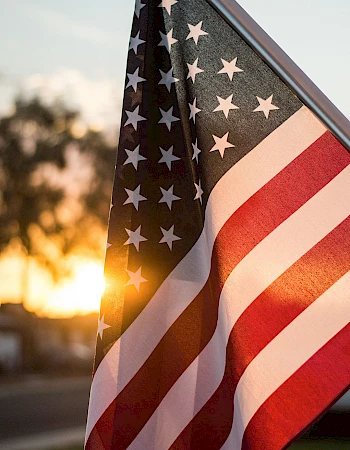 A waving American flag catching sunset light, stars and stripes glowing against a warm, golden backdrop.