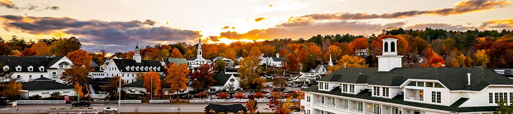 A picturesque lakeside town at sunset with autumn colors, featuring charming white buildings and a calm waterfront.