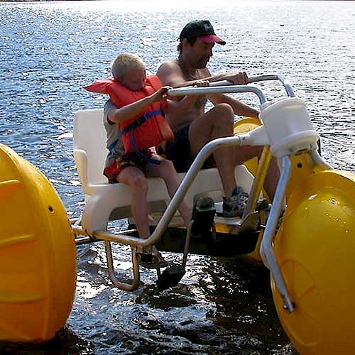 A man and a child are on a yellow water tricycle, pedaling on a lake with life vests on.