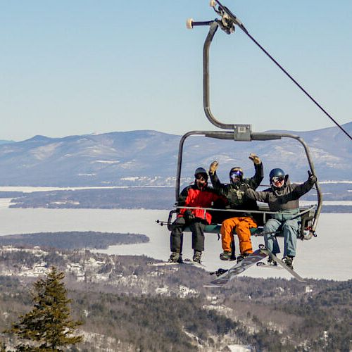 People are on a ski lift, enjoying scenic mountain views with snowy landscapes and evergreen trees in the background.