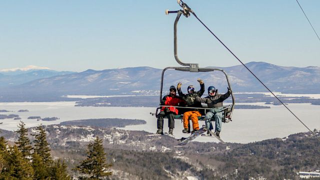 People are on a ski lift, enjoying scenic mountain views with snowy landscapes and evergreen trees in the background.