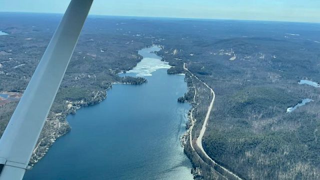 Aerial view of a winding river or lake surrounded by forested landscape with a road running alongside, seen from an airplane in flight.