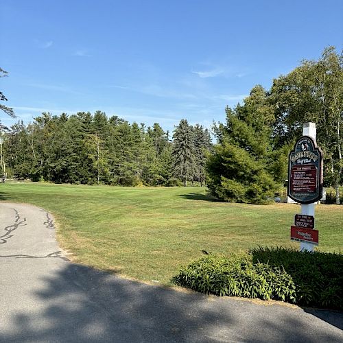 A paved path next to a lawn, trees, and a sign under a clear blue sky.