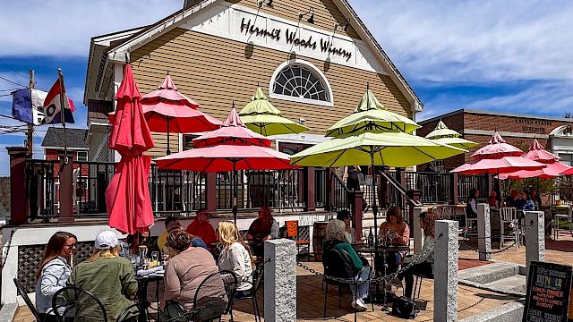 People dining outside a winery with colorful umbrellas and clear skies in the background.