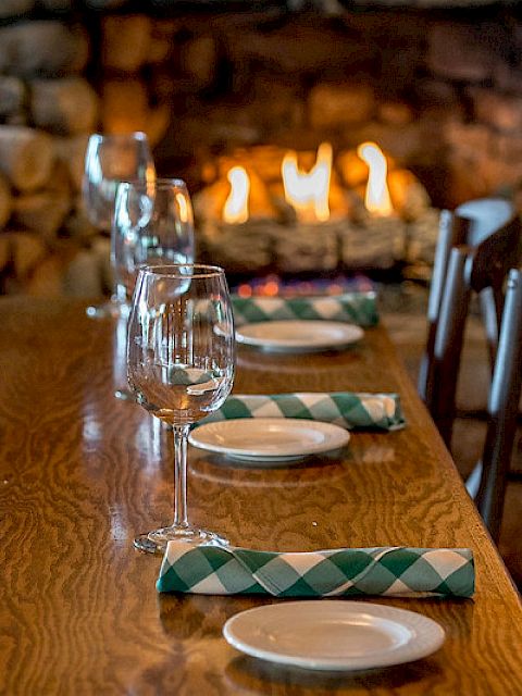 A dining table set with glasses, plates, and napkins in front of a cozy fireplace, creating a warm and inviting atmosphere.