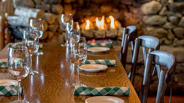 A dining table set with glasses, plates, and napkins in front of a cozy fireplace, creating a warm and inviting atmosphere.