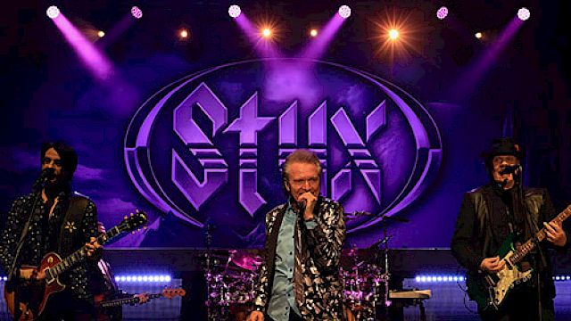 A band is performing on stage with colorful lights and a "Styx" logo in the background.